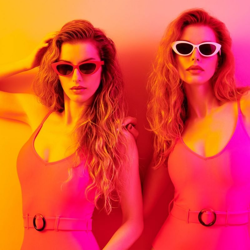 Fashion. Disco party woman have fun dance. Two girl in colorful neon light, sisters. Beautiful model, wet hair, makeup, in swimsuit, neon nightclub fashionable style. Pool summer party, creative art